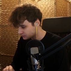 a young man sitting in front of a microphone with headphones on his ears and looking down