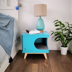 a blue nightstand next to a bed with a plant on it and a lamp in the corner