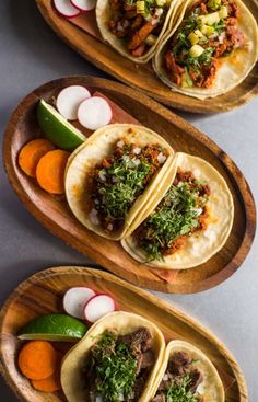 three tacos with meat and vegetables on wooden plates