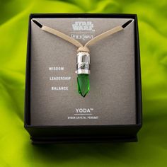 a star wars necklace is in a box on a green cloth covered table with the words yoda written below it