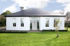 a white house sitting on top of a lush green field next to a small tree