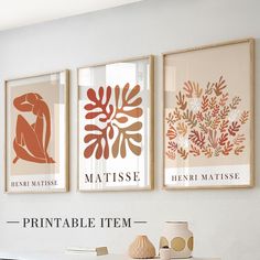 three framed art prints hang on the wall above a table with vases and books