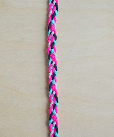 a pink, blue and black braided necklace on a wooden surface