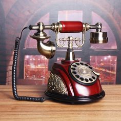 an old fashioned red phone sitting on top of a wooden table