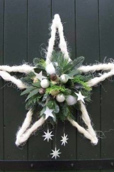 a christmas star decoration hanging on the side of a green building with white stars and greenery