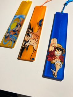 three cartoon bookmarks are sitting on a white table with blue string attached to them