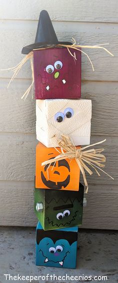 a stack of halloween blocks with faces painted on them and a witch's hat hanging from the top