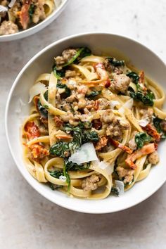 a white bowl filled with pasta and meat on top of a marble counter next to a plate of bread