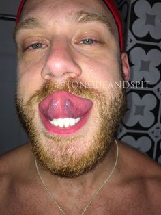 a man with his tongue out making a funny face while wearing a red hat and necklace