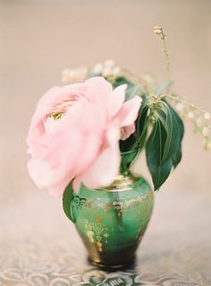 a green vase filled with pink flowers on top of a table