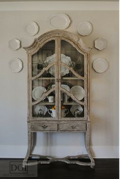 an old china cabinet with plates on the top and bottom, in front of a white wall