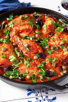 a skillet filled with meat covered in sauce and garnished with olives