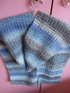 a blue and gray knitted sweater hanging from a hook on a pink door handle