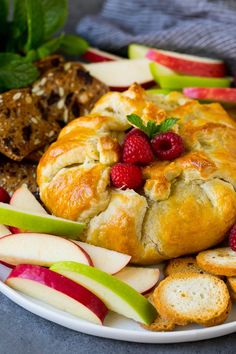 an apple and raspberry pastry on a plate next to sliced apples, bread and cookies