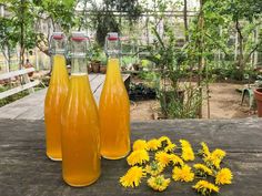 three bottles filled with liquid sitting on top of a wooden table next to yellow flowers