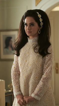 a woman with long hair wearing a white dress and flower in her hair, looking at the camera