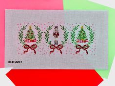 a cross stitch christmas card with three small trees and bows on the front, in red green and pink