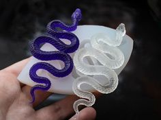 a hand holding a white and purple snake on top of a piece of plastic in front of a black background