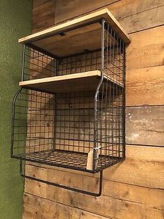 a metal wire shelf with two shelves on the top and one shelf below it, against a wooden wall