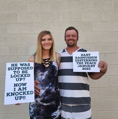 two people holding signs in front of a brick wall