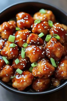 a black bowl filled with sesame chicken and garnished with green onions on top