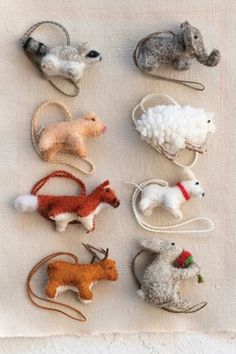 several small toy animals are sitting on a table cloth with white linen behind them and one has a red flower in its hair