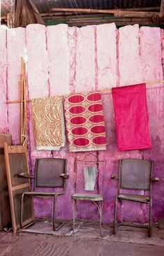 three chairs are sitting in front of a pink wall with towels hanging on the clothesline