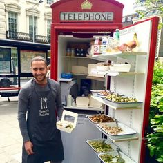 a man standing in front of a phone booth filled with food and drinks, smiling at the camera