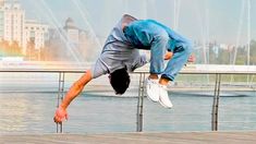 a man is doing a handstand on a wooden deck near water and buildings