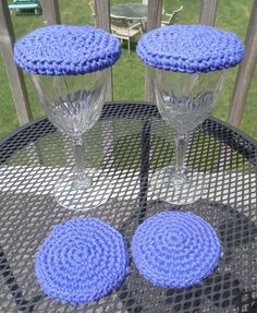 two wine glasses sitting on top of a table next to each other with blue crocheted coasters