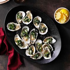 a black plate topped with lots of oysters next to a bowl of lemon wedges