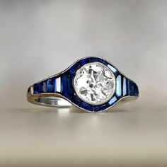 an antique diamond and blue enamel ring on a white surface with the center surrounded by diamonds