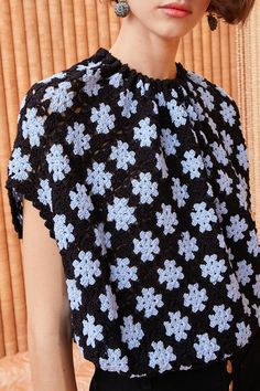 a woman with short hair wearing a black and white crochet top that has blue flowers on it