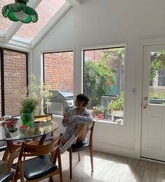 a woman sitting at a table in front of two large windows looking out onto the back yard