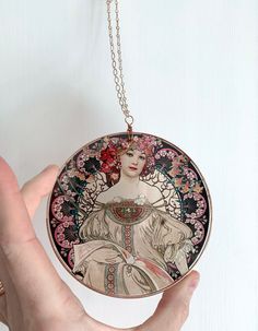 a hand holding a necklace with an image of a woman in a dress on it