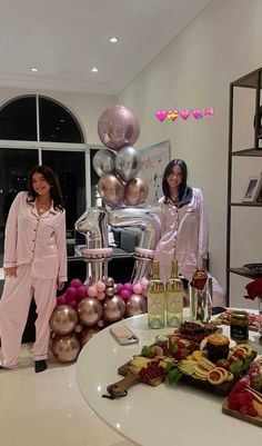 two women in pink pajamas standing next to a table with food and drinks on it