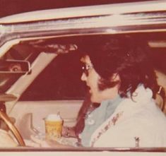 a woman sitting in the back seat of a car holding a drink and looking at another person