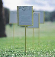 three yellow and white signs in the grass with trees in the backgrounnd