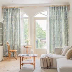 a living room filled with furniture next to a window covered in blue and white curtains