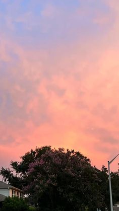 the sky is pink and blue as the sun goes down over some trees in front of a house