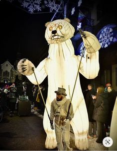 a man standing next to a giant polar bear float in the street with people looking on