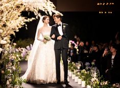 a bride and groom standing in front of an audience at a wedding ceremony with flowers on the aisle