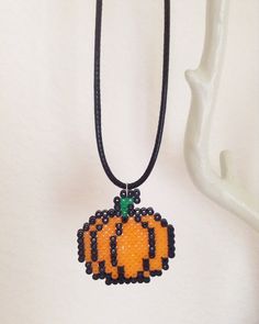 an orange beaded pumpkin with black beads on a black leather cord is hanging from a white mannequin