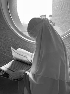 a woman reading a book in front of a round window with a white veil on her head