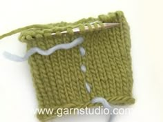 a green knitted object with white yarn on the side and a knitting needle in the middle