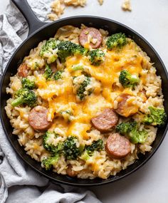 a skillet filled with rice, sausage and broccoli on top of a table