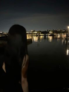 a woman standing in front of a body of water at night with the lights on