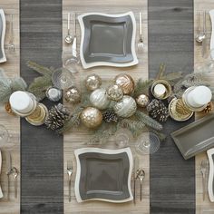 the table is set for christmas dinner with silver and gold plates, silver cutlery, pine cones, white dishes