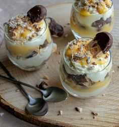 four desserts in small glass dishes with spoons on a wooden tray next to each other