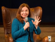 a woman sitting in a chair holding a microphone and making the peace sign with her hands